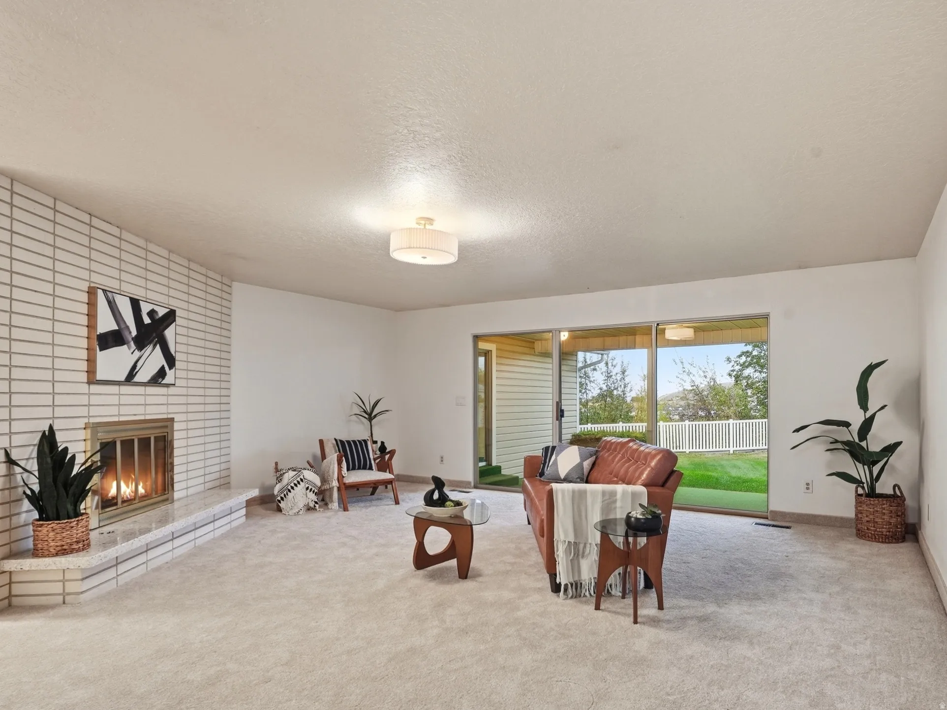 White brick fireplace with hearth, plush carpet, sliding glass door, and backyard
