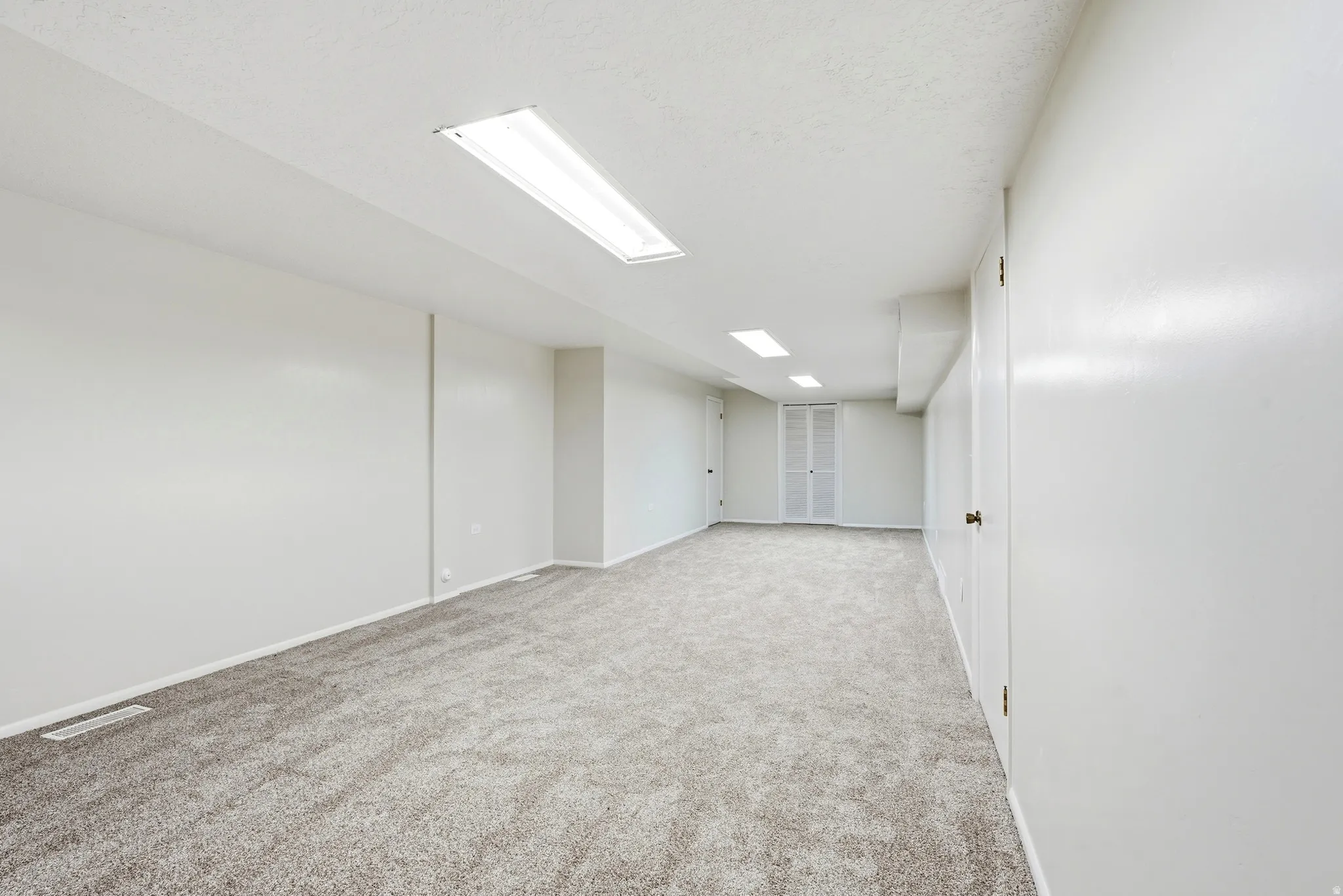 Spacious room featuring neutral carpeting, white painted walls, and built-in overhead lighting