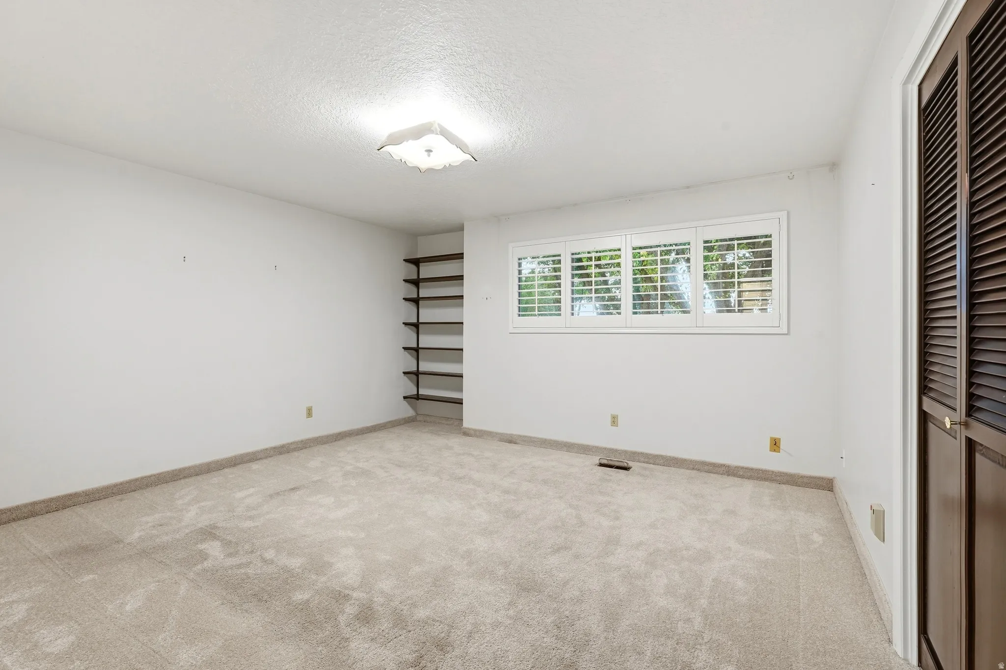 Recessed built-in shelving, windows with plantation shutters, light-colored carpeting, white walls, and a ceiling-mounted light fixture