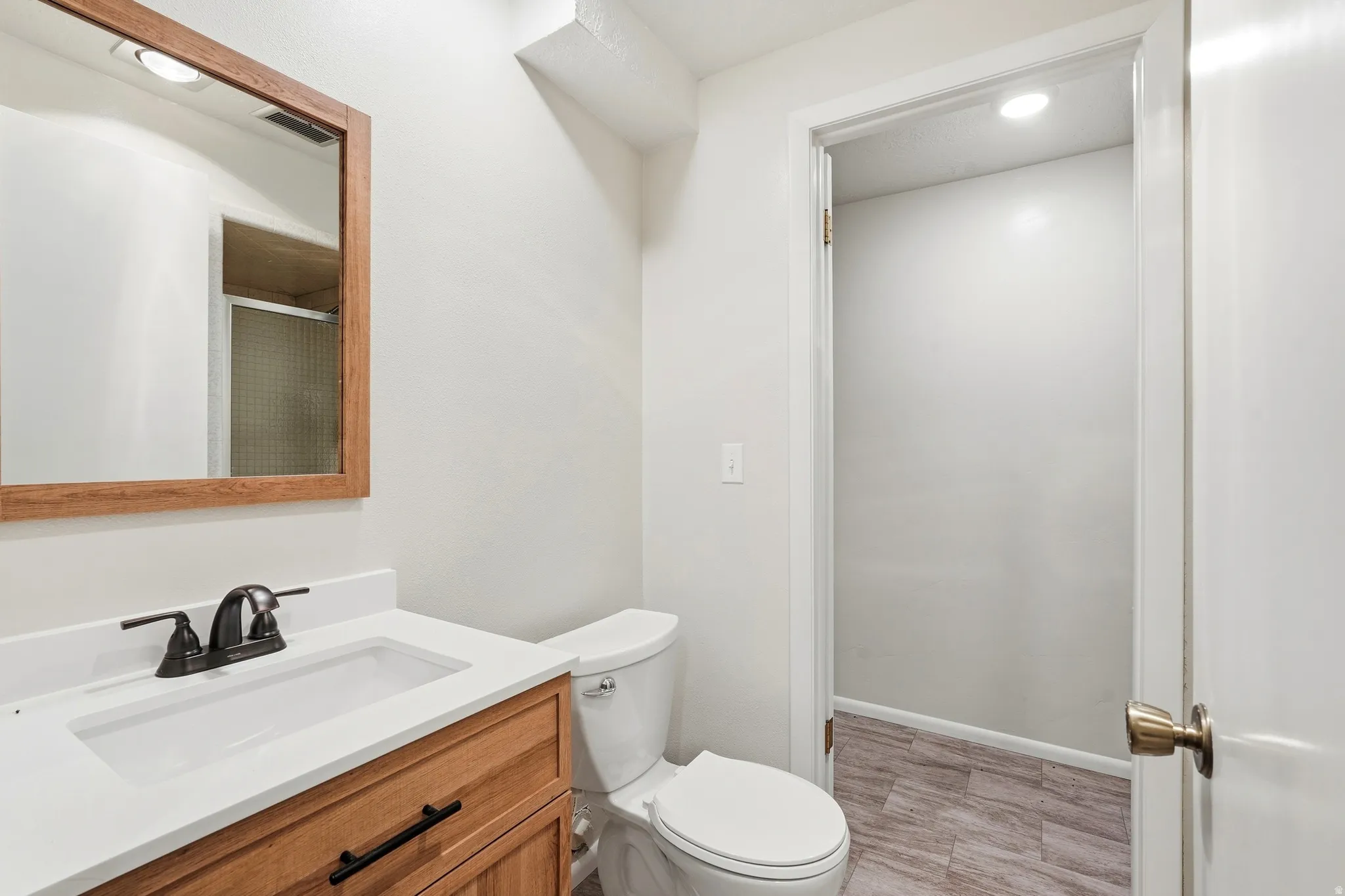 Bathroom featuring a wood-finish vanity with an integrated white sink, bronze-finish faucet, and coordinating wood-frame mirror