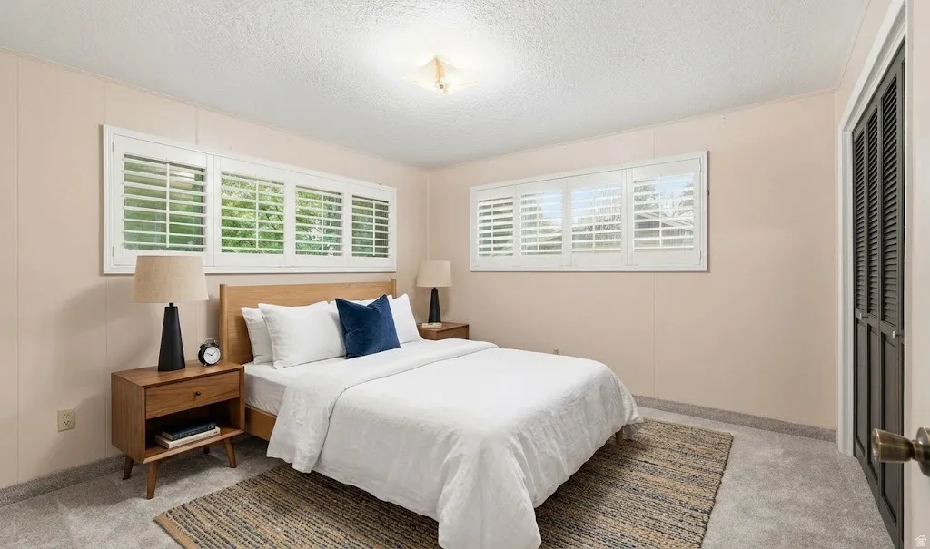 Two windows with white plantation shutters, light wood-tone headboard, and a dark louvered bi-fold door