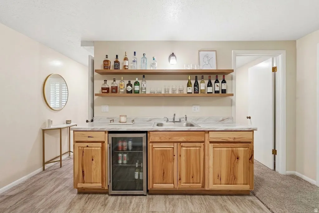 Wet bar with wood cabinetry, light-toned countertop, and integrated beverage refrigerator