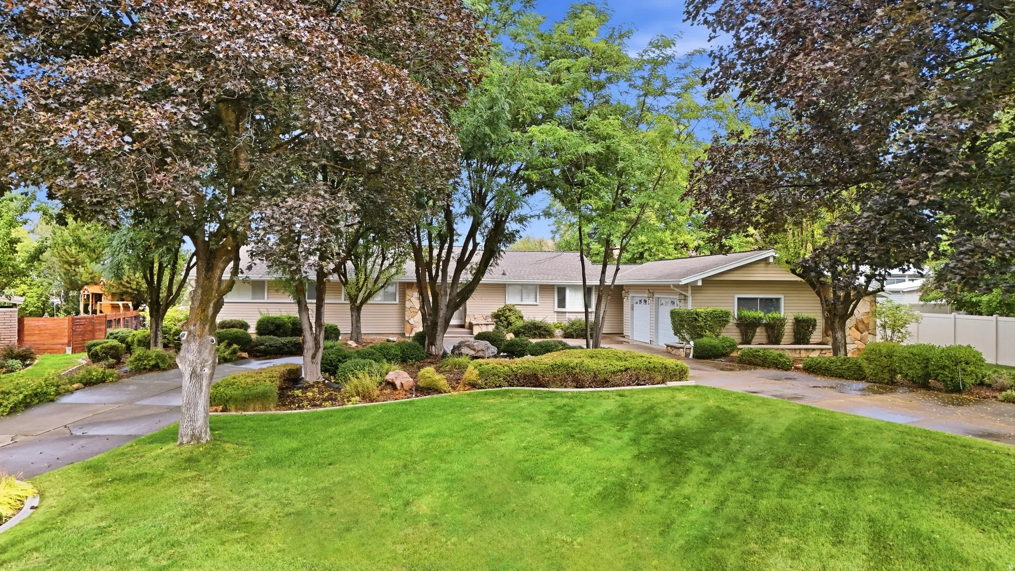 Manicured front lawn with mature trees, extensive landscaping, and a paved driveway