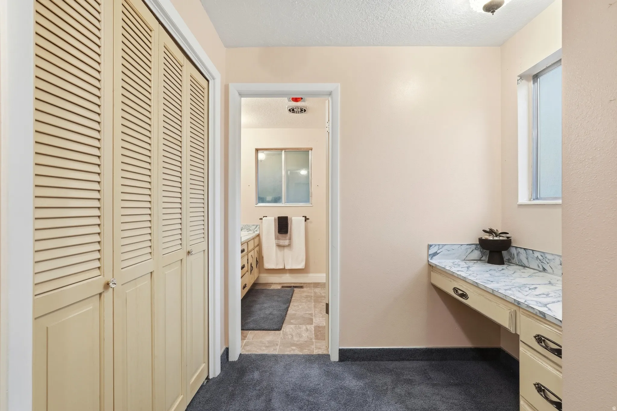 Louvered bi-fold doors, built-in vanity with a marbled countertop, and a window with frosted glass