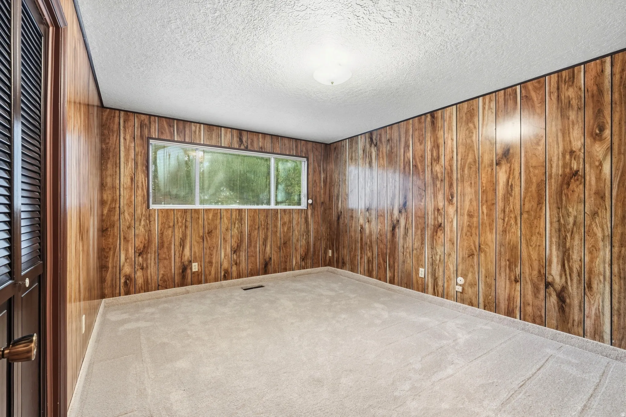 Wall paneling, light carpeting, louvered closet door, and a horizontal window