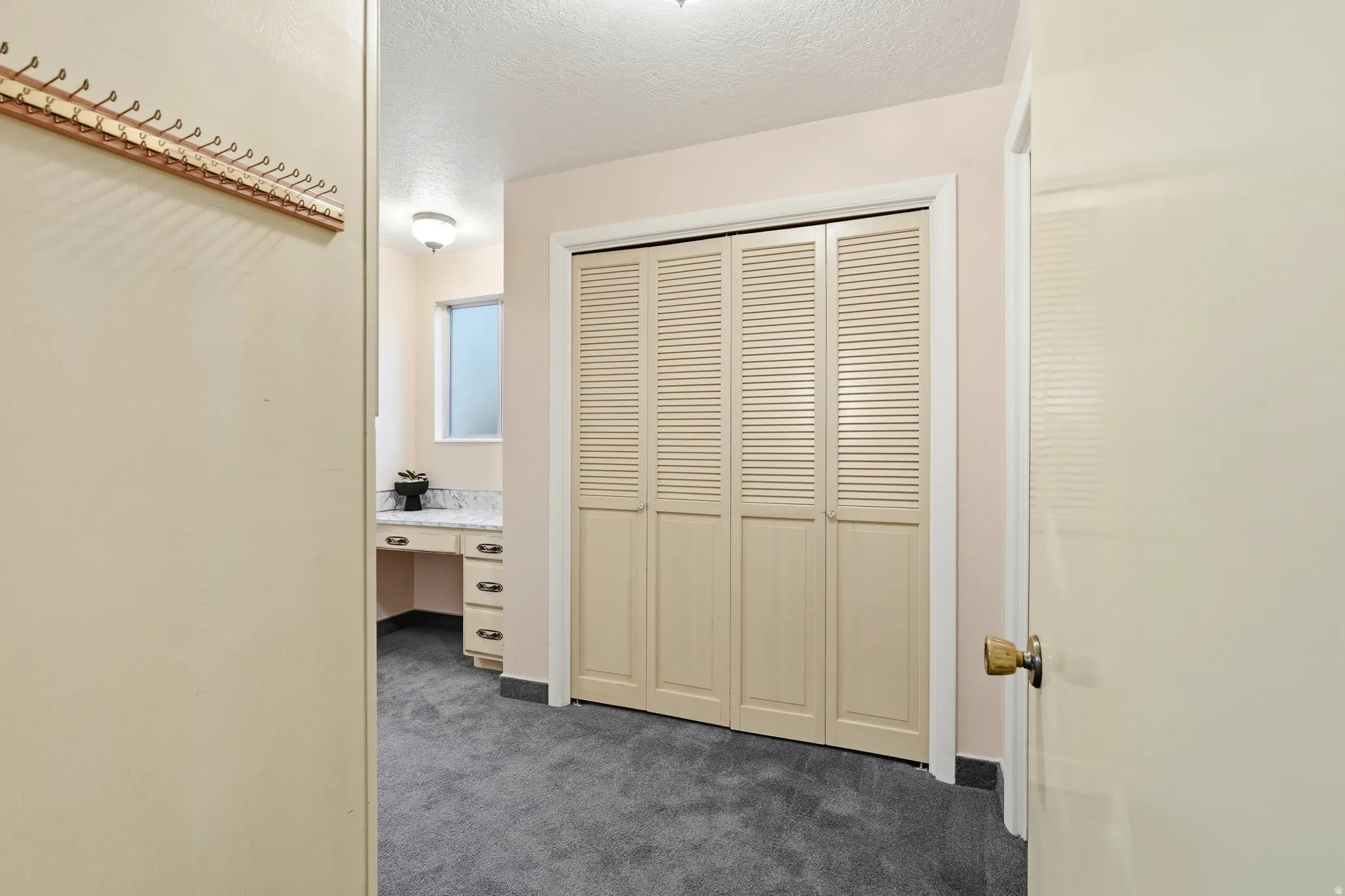 Built-in vanity with a light-colored countertop, louvered bi-fold closet doors, and recessed window