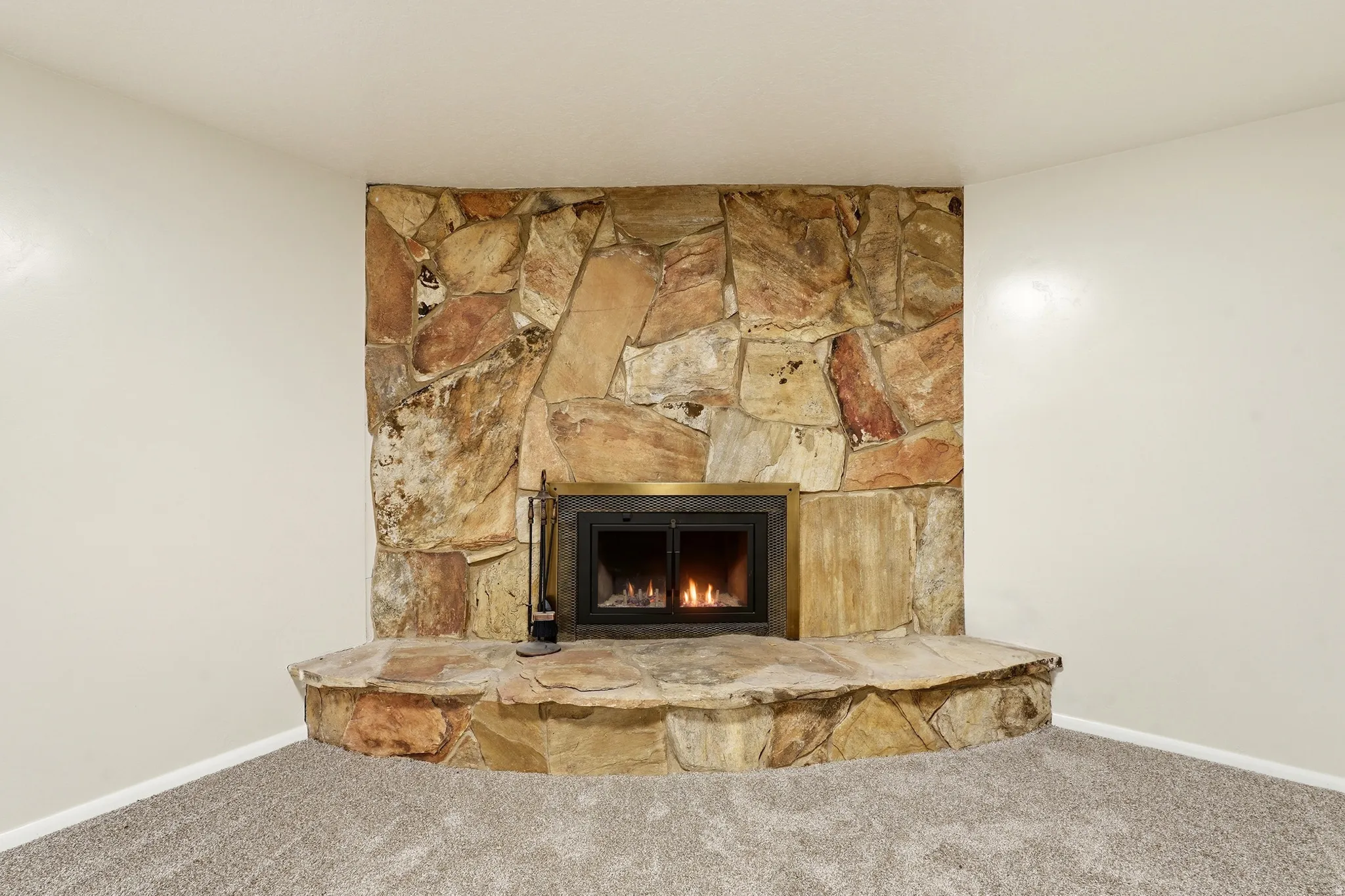 Stone-clad fireplace with a brass-framed firebox and a wide stone hearth, complemented by wall-to-wall carpeting