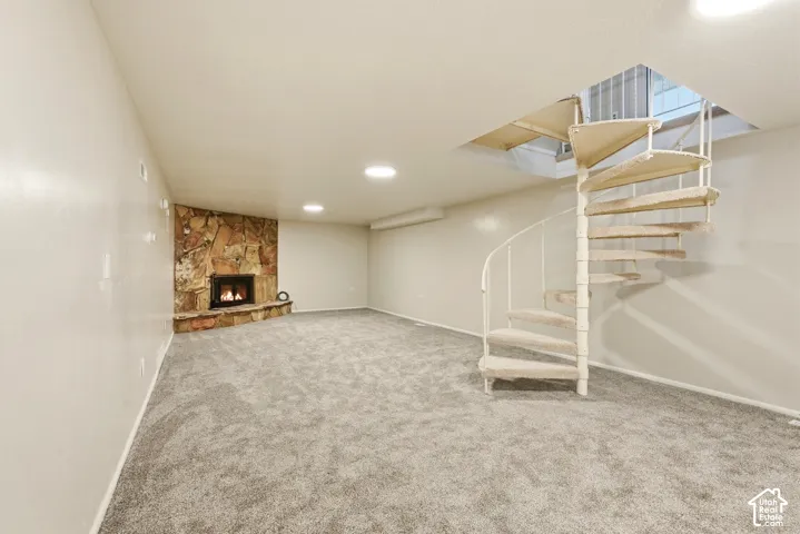 Spiral staircase, recessed lighting, corner stone-clad fireplace, and neutral carpeting
