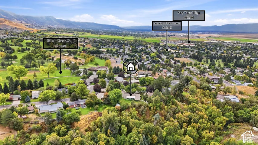 Aerial perspective of a verdant landscape featuring a residential area, a golf course, and distant mountains