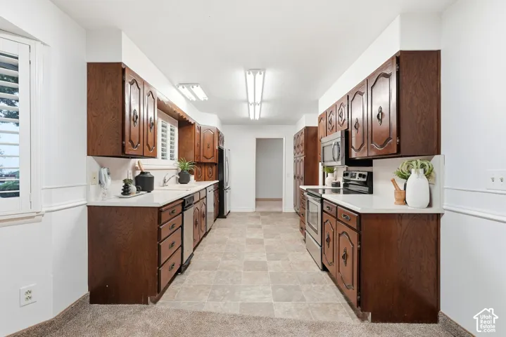 Galley kitchen with wood-finish cabinetry, white countertops, and stainless steel appliances