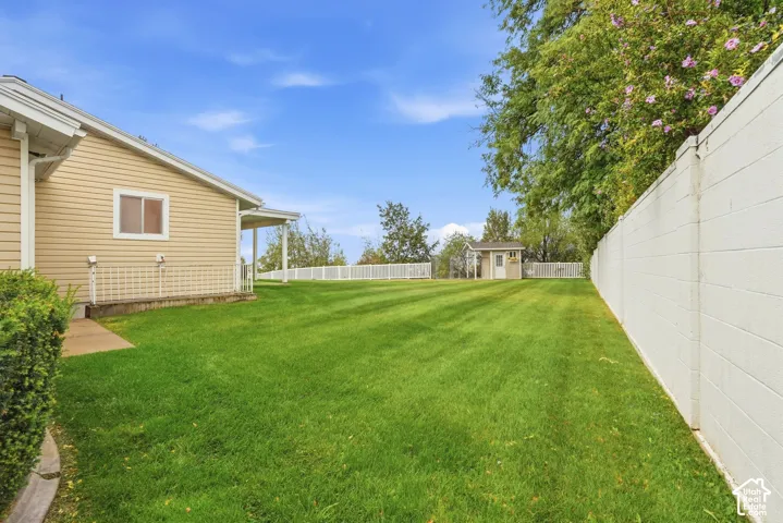 Expansive backyard featuring a meticulously manicured lawn, mature shade trees, and white vinyl fencing