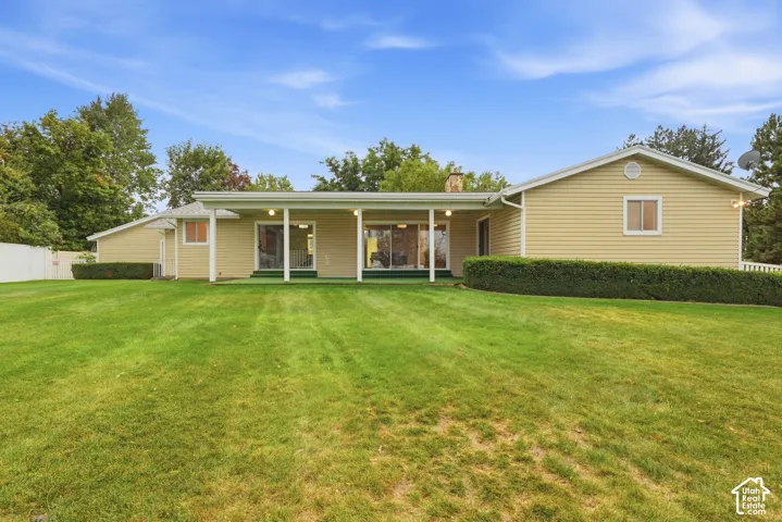 Spacious lawn area with a covered patio featuring multiple sliding glass doors and white columns