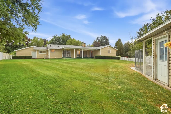 Expansive lawn with a white picket fence, mature trees, a covered patio, and a separate outbuilding