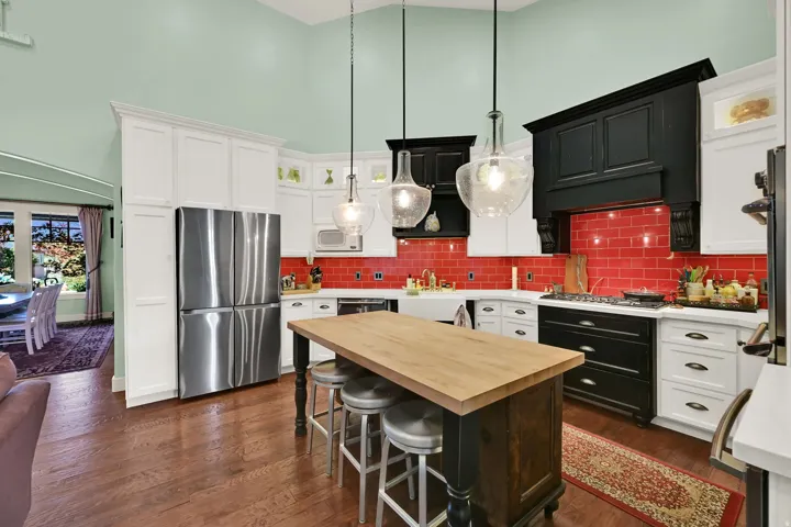 Chef's kitchen featuring white cabinetry with black accents, stainless steel refrigerator, gas cooktop, and a vibrant red subway tile backsplash