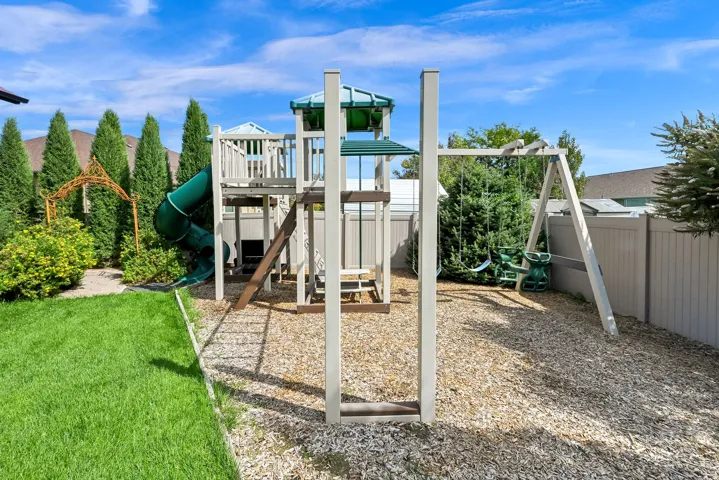 Expansive backyard featuring a manicured lawn, playground structure with slide and swings, wood chip ground cover, and a privacy fence