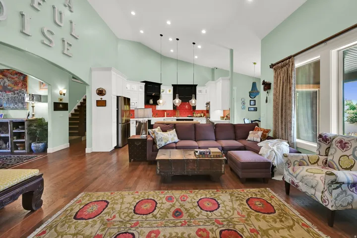 Vaulted ceiling with recessed lighting, wood-finish flooring, white cabinetry, stainless steel refrigerator, and a red tile backsplash