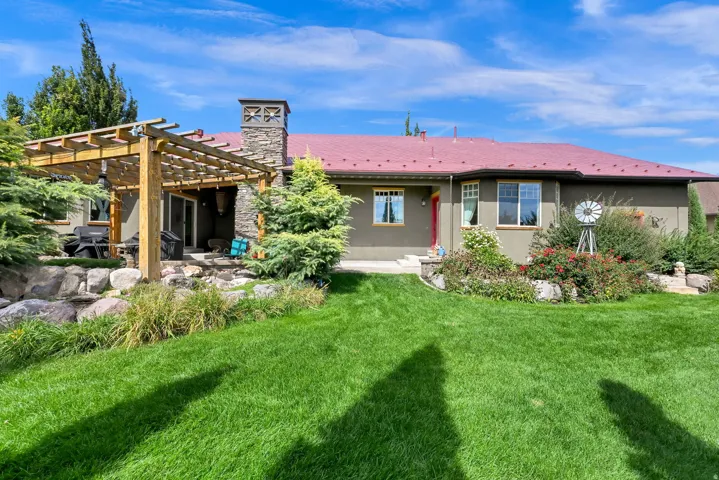 Expansive backyard featuring a manicured lawn, established landscaping, and a wood pergola over a patio