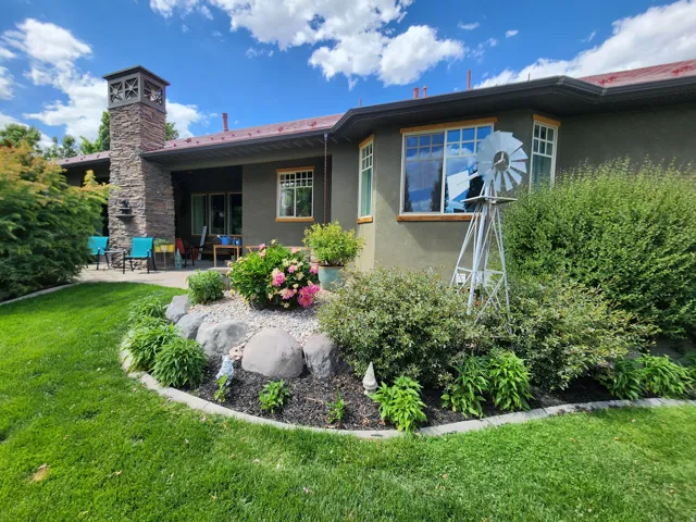 Expansive backyard featuring a manicured lawn, stone-clad chimney, stucco exterior, and a paved patio area