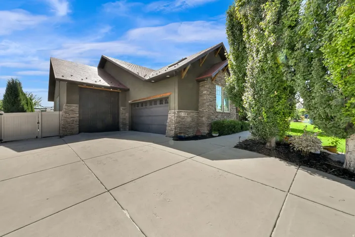 Exterior featuring a multi-panel garage door, stacked stone accents, a concrete driveway, and mature trees
