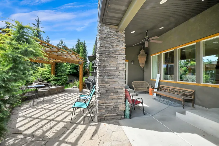 Expansive outdoor living area featuring a stone patio, large wood pergola, and mature landscaping