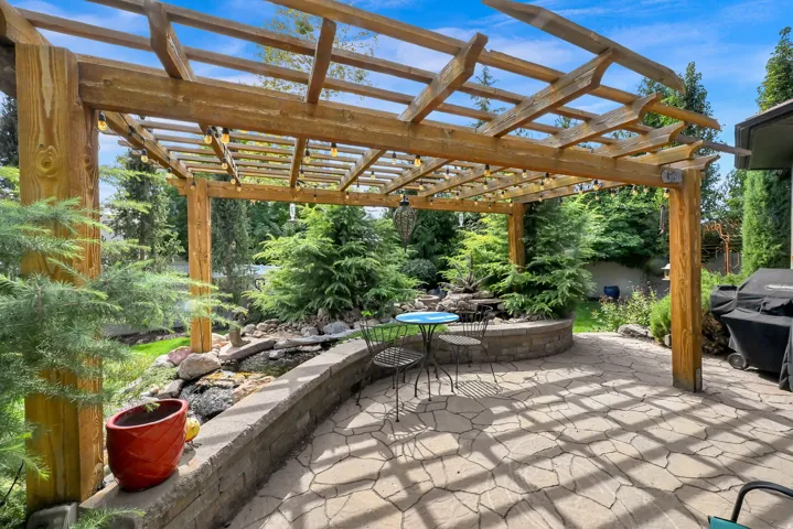 Expansive outdoor patio featuring a wood pergola, string lighting, flagstone paving, a stone retaining wall, and a water feature