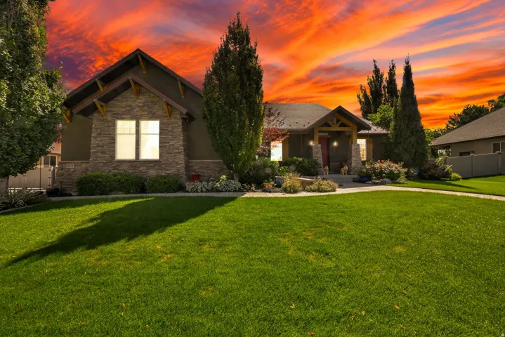 Stone façade accents, gabled roofline, covered entry, established landscaping, and expansive lawn
