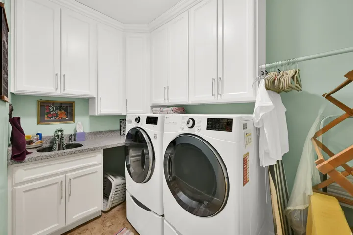 White upper cabinetry, white lower cabinetry, dark stone-finish countertop, integrated sink, and white wall-mounted hanging rod