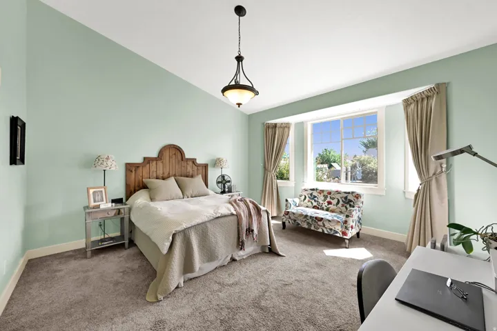 Vaulted ceiling with an attached pendant light, bay window with white trim, and light green wall paint