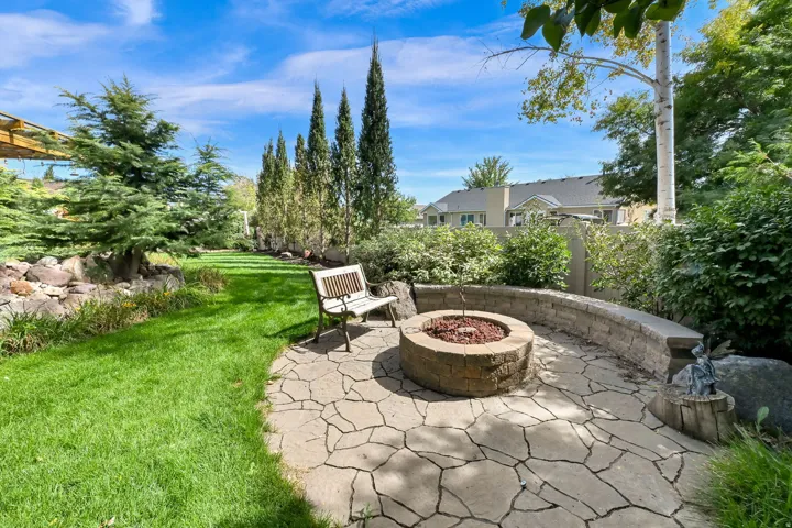 Expansive backyard featuring a manicured lawn, established landscaping, and a flagstone patio with a built-in fire pit and retaining wall