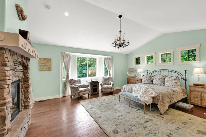 Vaulted ceiling with a chandelier, stone fireplace, wood-finish flooring, bay window, and transom windows