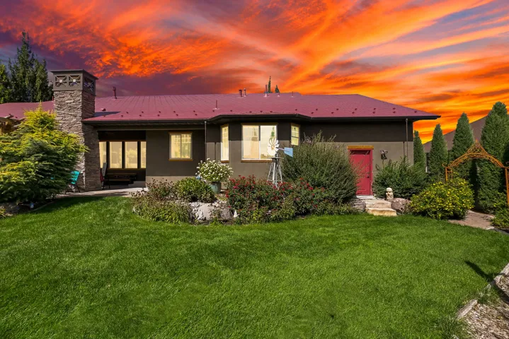 Expansive green lawn, mature landscaping, stone chimney, red entry door, and metal roofing