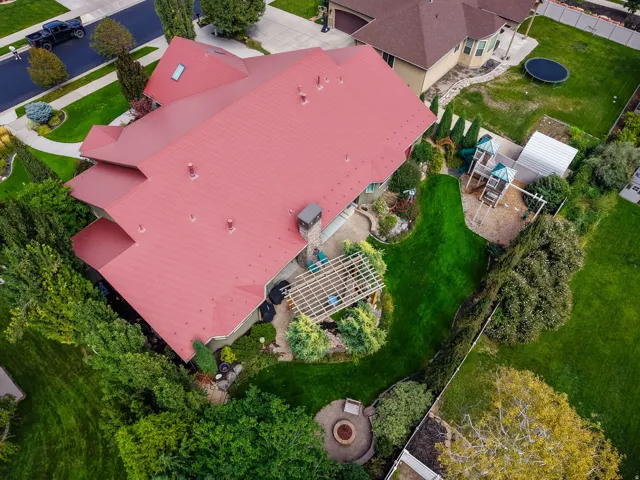 Red metal roof, expansive green lawn, built-in fire pit area, pergola-covered patio, established perimeter landscaping