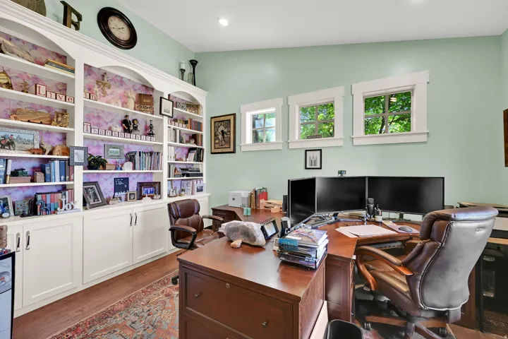Built-in white cabinetry with arched details, wood-finish flooring, and multiple windows with white trim