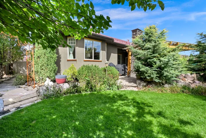 Backyard featuring a manicured lawn, established landscaping, and a stone patio