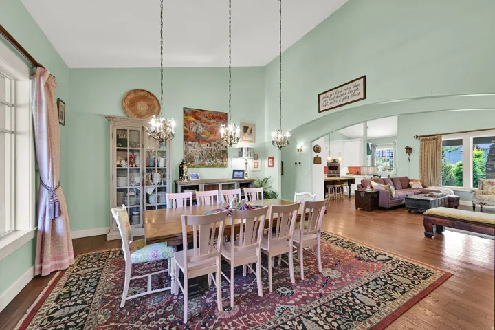 Dining area featuring dual chandeliers, high ceilings, arched entryway, and wood-finish flooring