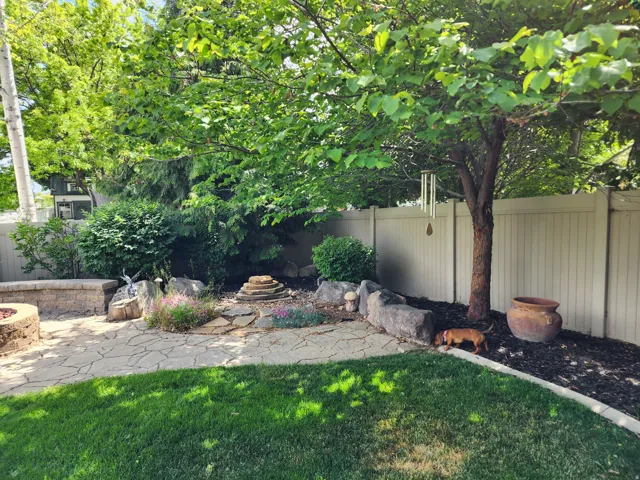Expansive yard featuring a manicured lawn, flagstone patio, built-in fire pit, and mature trees
