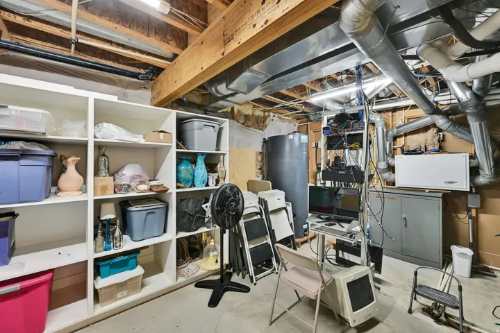 Basement with exposed wood ceiling joists, concrete flooring, built-in shelving, and utility systems