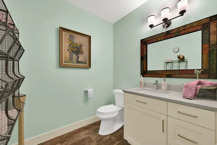 Vanity with a light-toned countertop and an integrated sink, wood-finish flooring, a wall-mounted light fixture, and a toilet