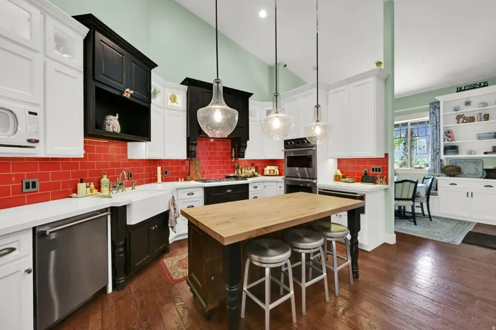 Kitchen featuring a central island with a wood countertop, white shaker-style cabinetry, and a red subway tile backsplash