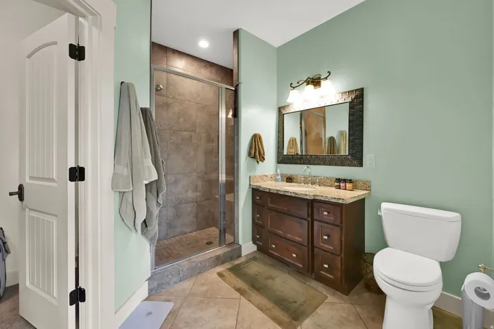 Spa-inspired primary bathroom featuring a wood-finish vanity with dual sinks and quartz countertop, slate-tiled walk-in shower with frameless glass enclosure, and soft sage green walls