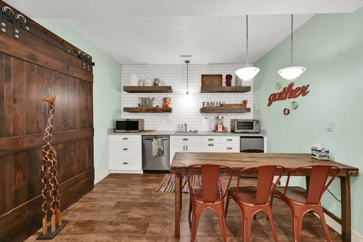 Wood-finish flooring, white subway tile backsplash, white cabinetry with dark hardware, gray countertop, and a dark wood barn door