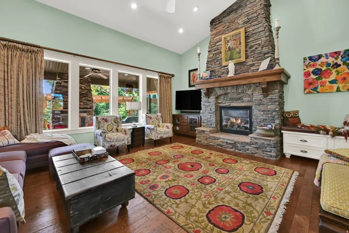 Stone-faced fireplace with a wood mantel, wood-finish flooring, and vaulted ceiling