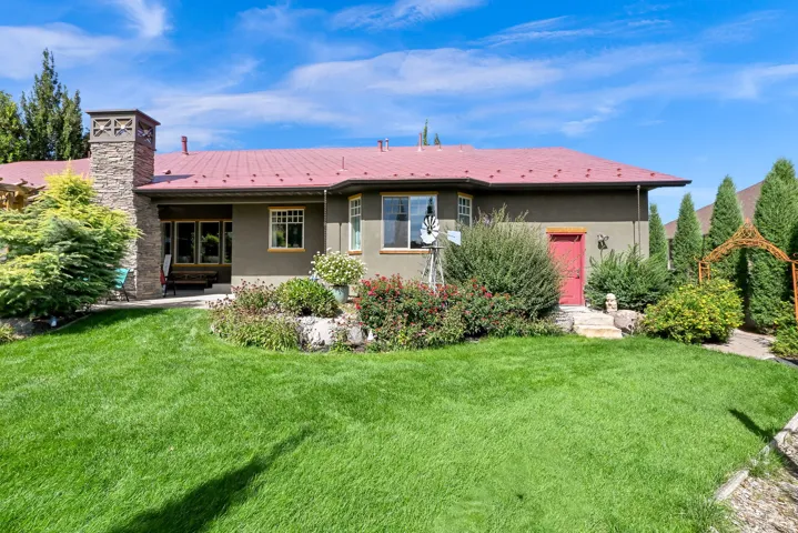 Expansive green lawn with mature landscaping, a stone-clad chimney, and a red metal roof