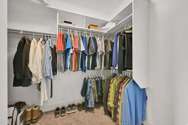 Walk-in closet featuring white built-in shelving, white hanging rods, and neutral-toned carpeting