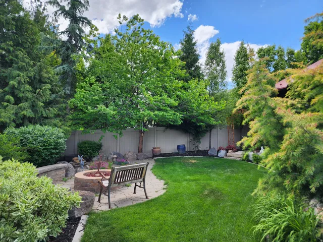 Lush backyard featuring a manicured lawn, stone paver patio, built-in stone fire pit, and mature perimeter landscaping