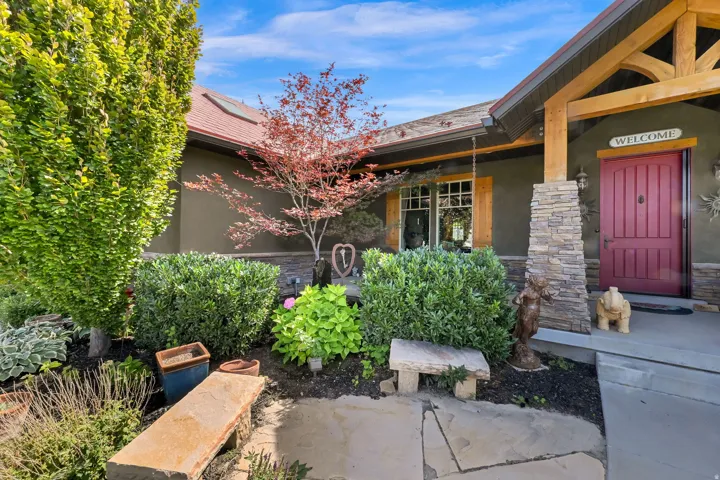 Stucco exterior with a red door, stone veneer column, exposed wood beam accents, and mature landscaping
