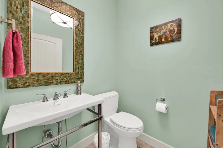 Pedestal sink with chrome fixtures, mosaic-framed mirror, and a white toilet