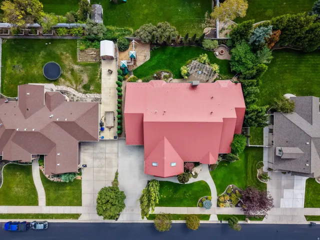 Expansive property featuring a red metal roof, concrete driveways, mature landscaping, and a manicured lawn