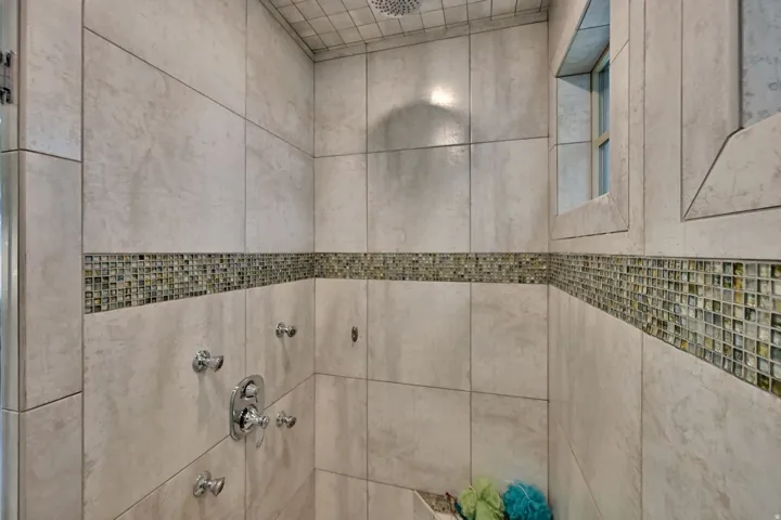 Tiled shower with a mosaic tile accent band, recessed window, and ceiling-mounted rain shower head