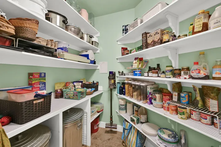 Spacious pantry featuring multiple tiers of white shelving, built-in lower countertops, and light green painted walls